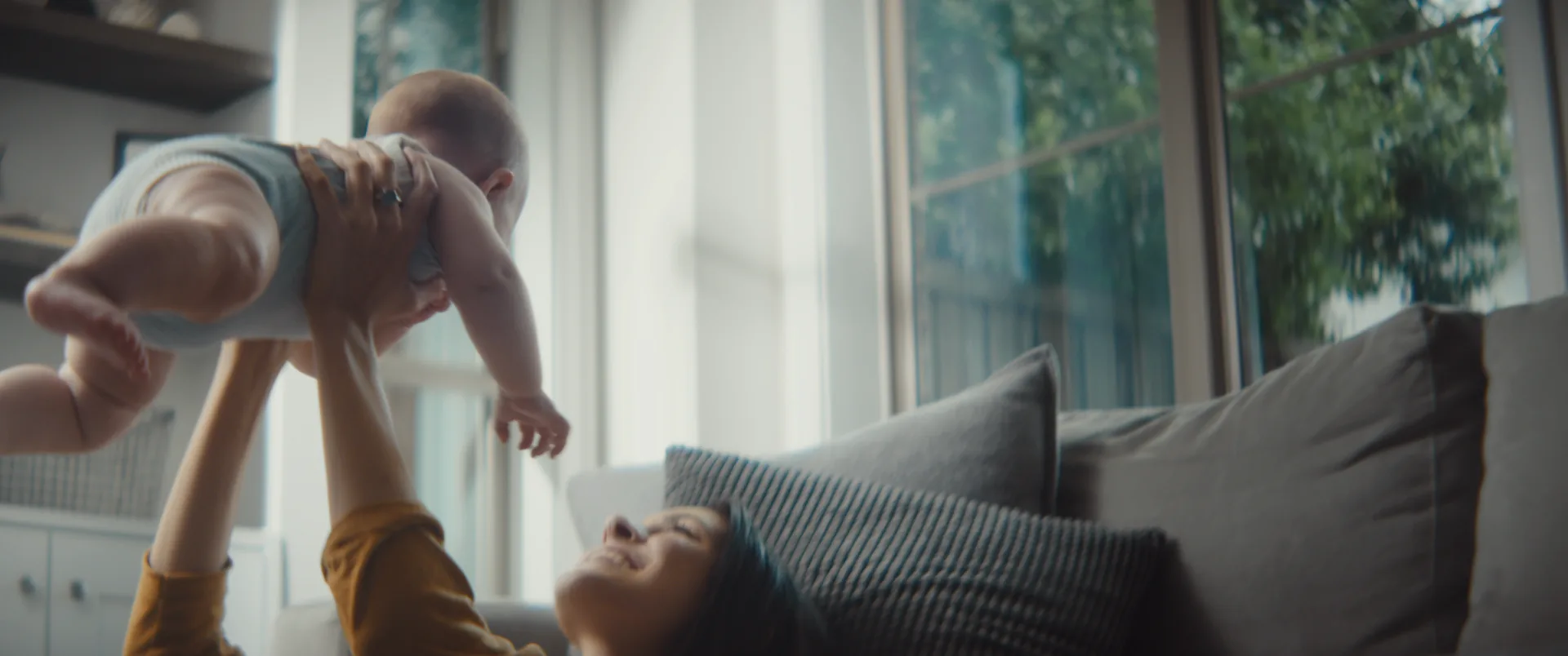 A mother lying on the couch lifting her baby into the air