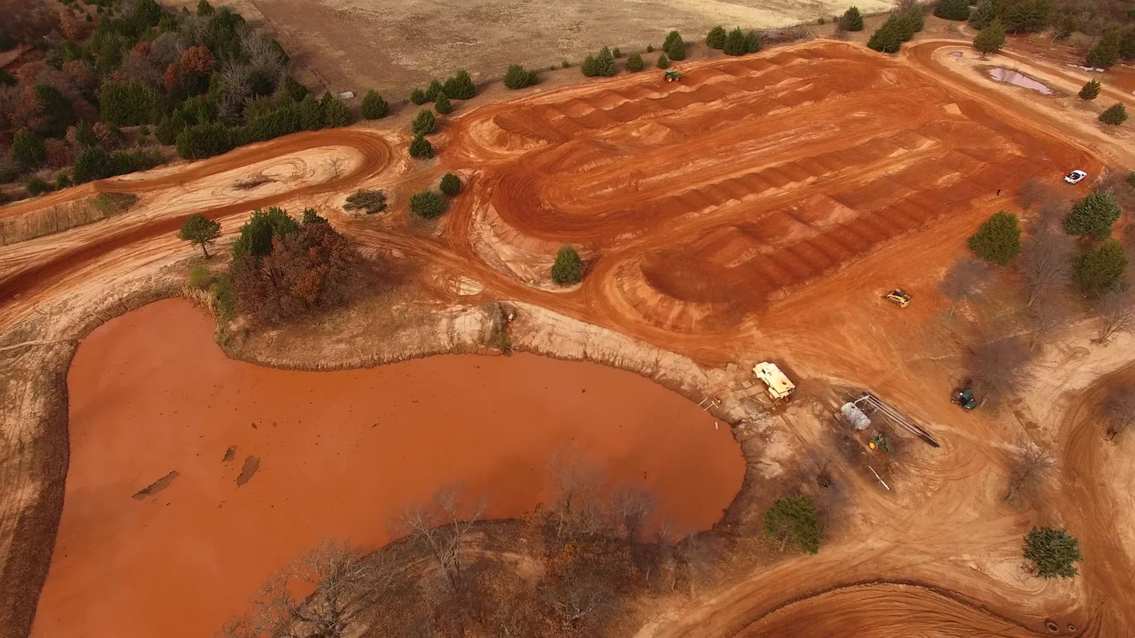 Wide aerial of a red-dirt motocross track and pond