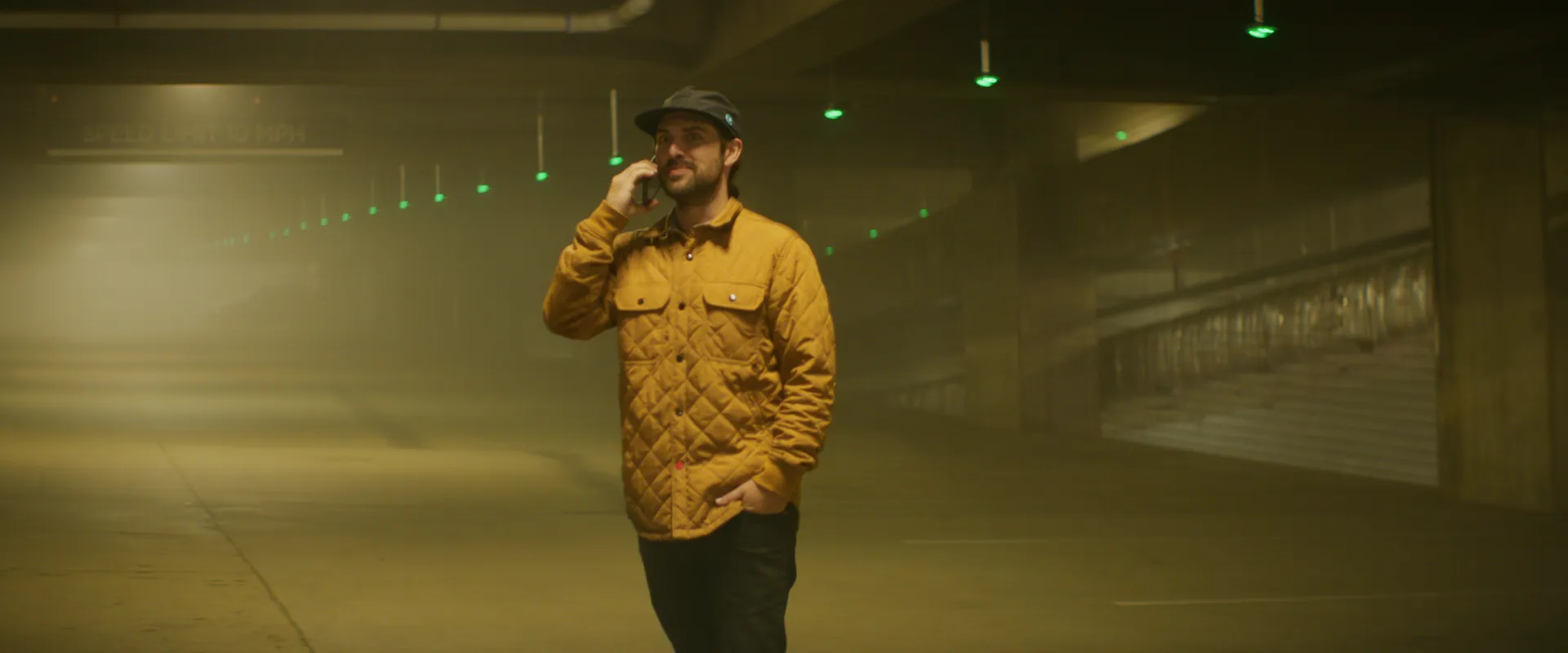 A man in a mustard quilted jacket on a phone call in a fog-filled parking garage
