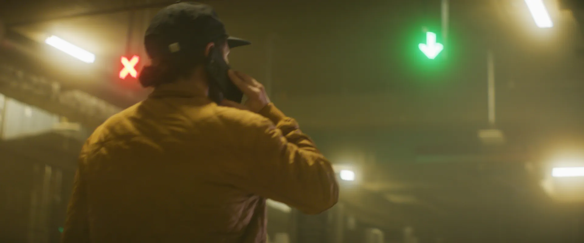 Over the shoulder of a man on the phone, red and green lane signals glowing through garage fog