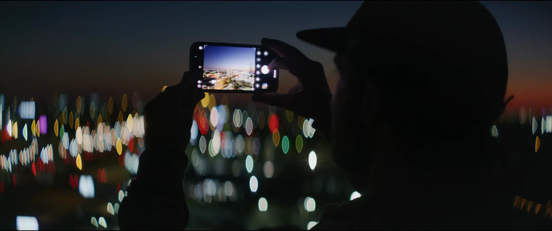 Hands framing the skyline on a phone screen, the real city lights blurred behind it