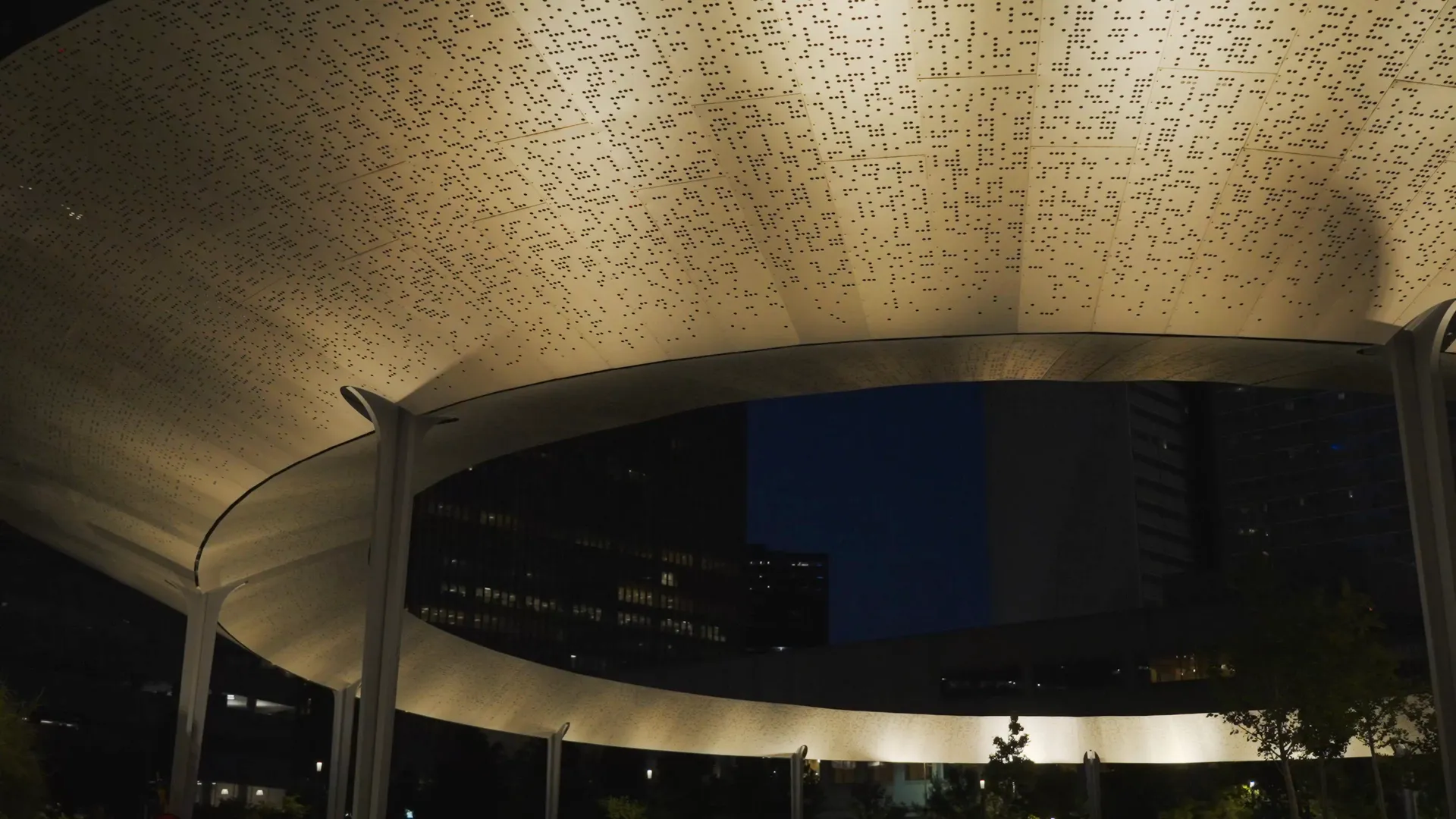 A perforated metal canopy lit from below at night