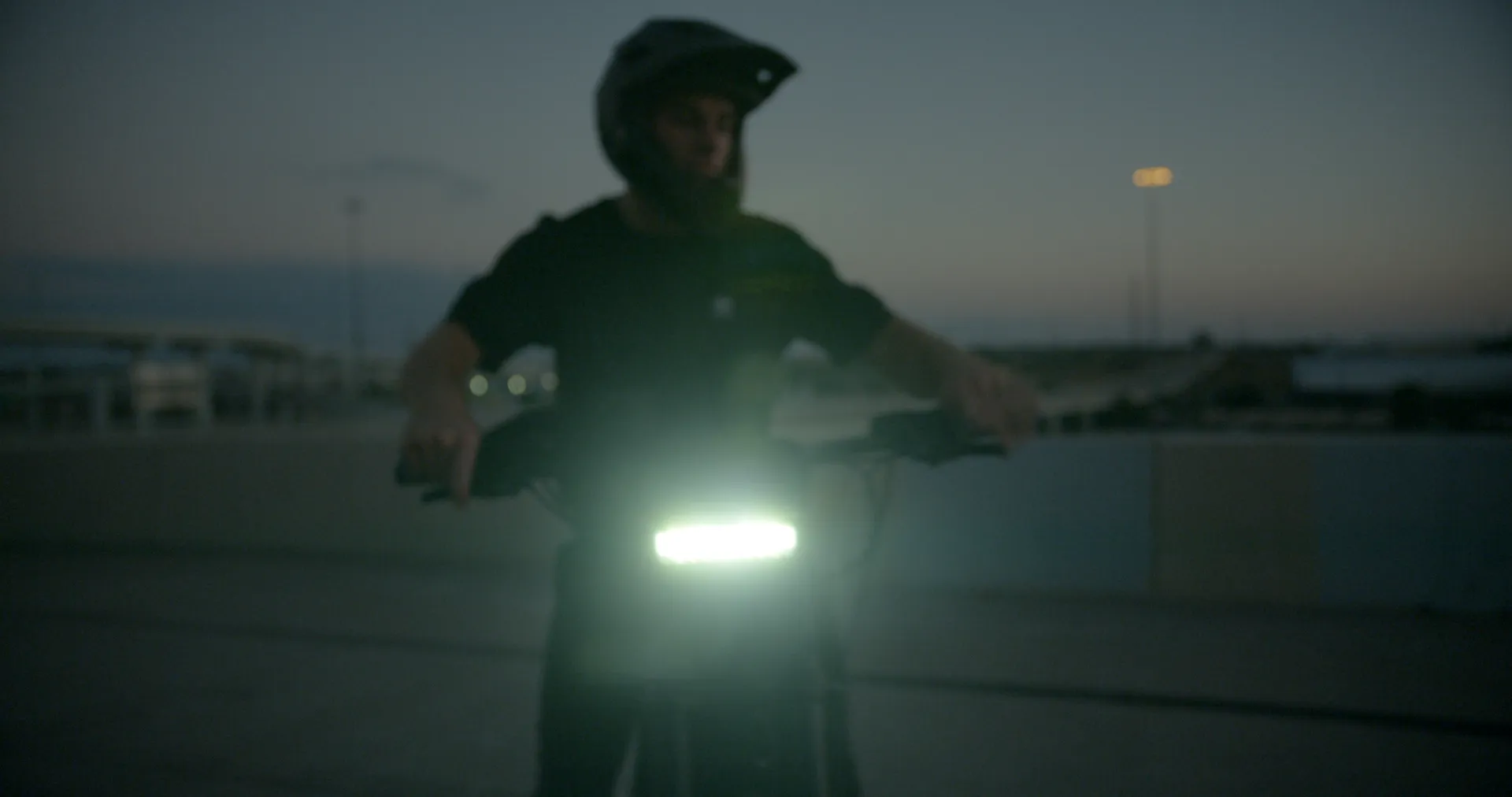 A rider facing the camera behind a bright headlight at dusk