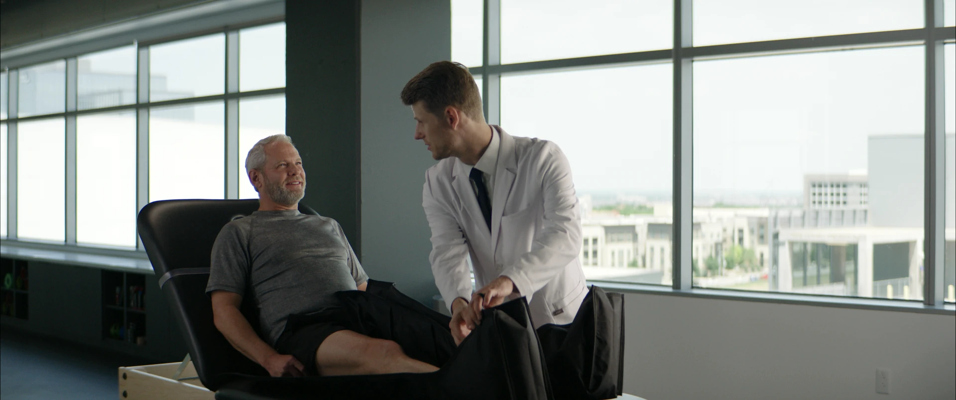 An older patient relaxing in compression boots while his doctor checks the fit