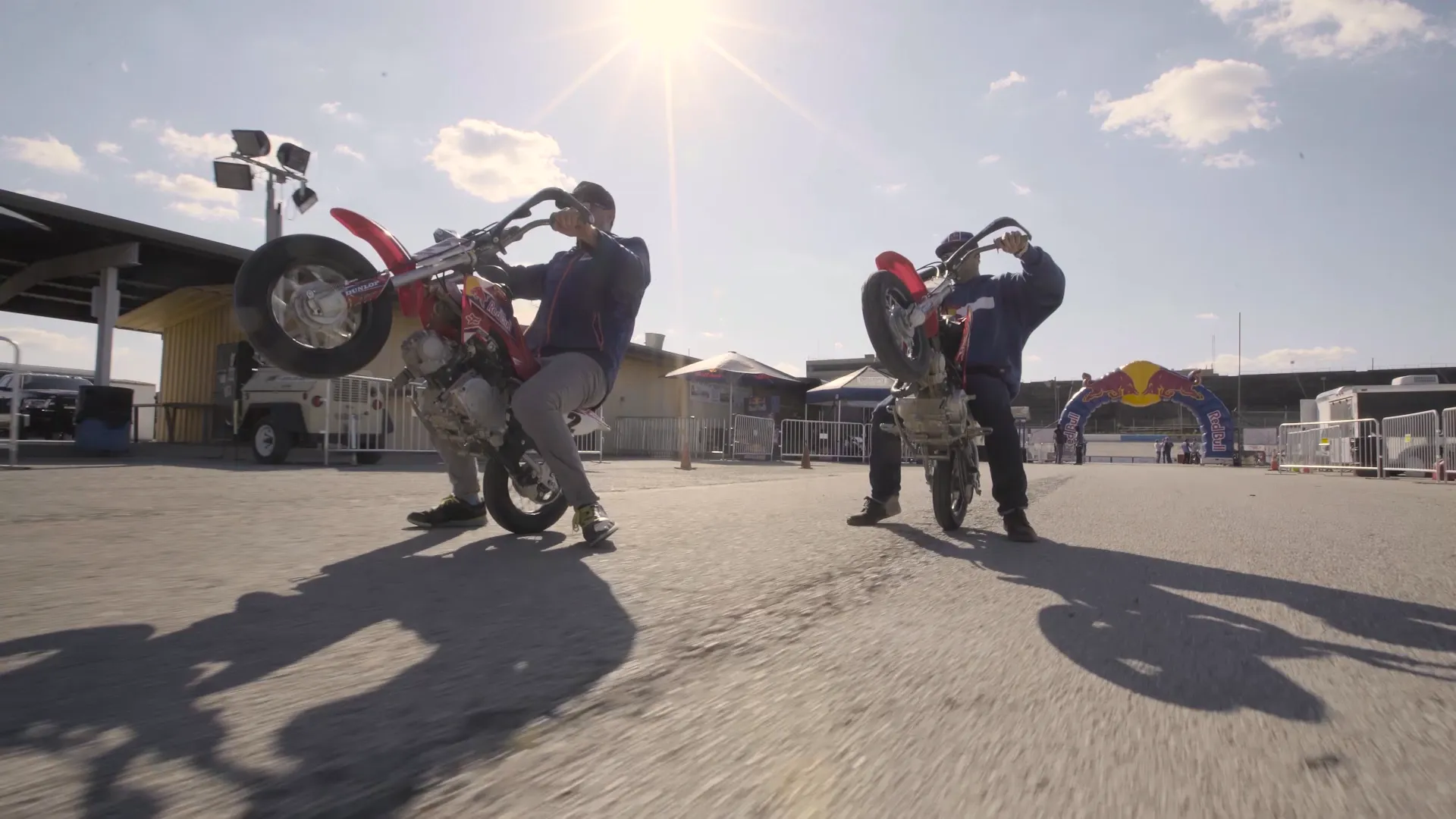 Two riders pulling wheelies with the sun behind them