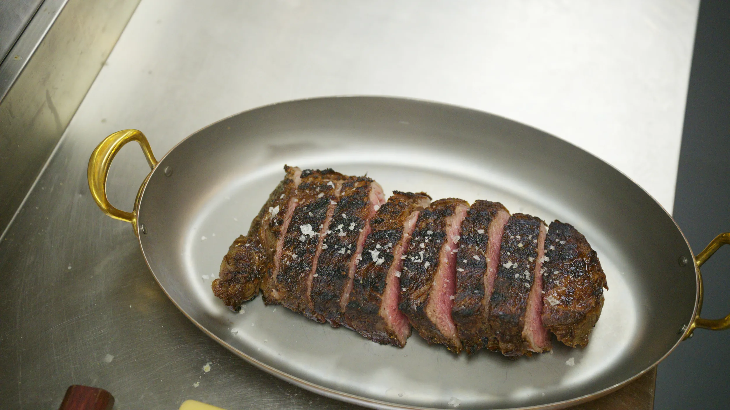 Sliced Senku wagyu strip with flaky salt in a copper oval pan