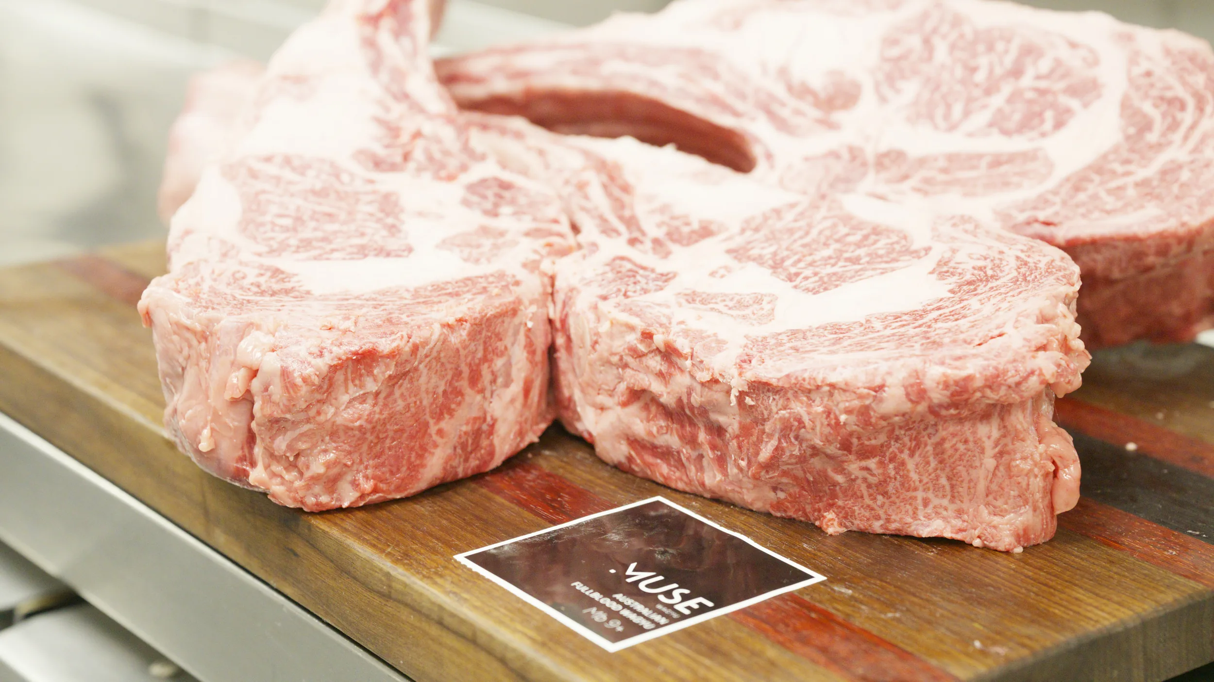 Raw marbled tomahawk steaks on a walnut board with a MUSE card