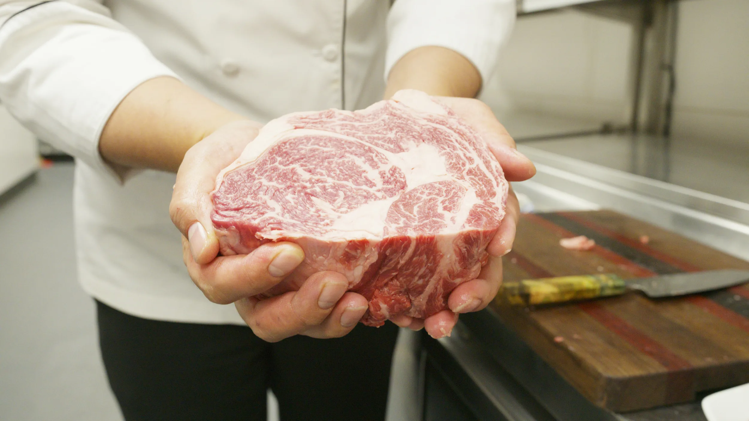 Chef's hands holding a thick raw marbled ribeye