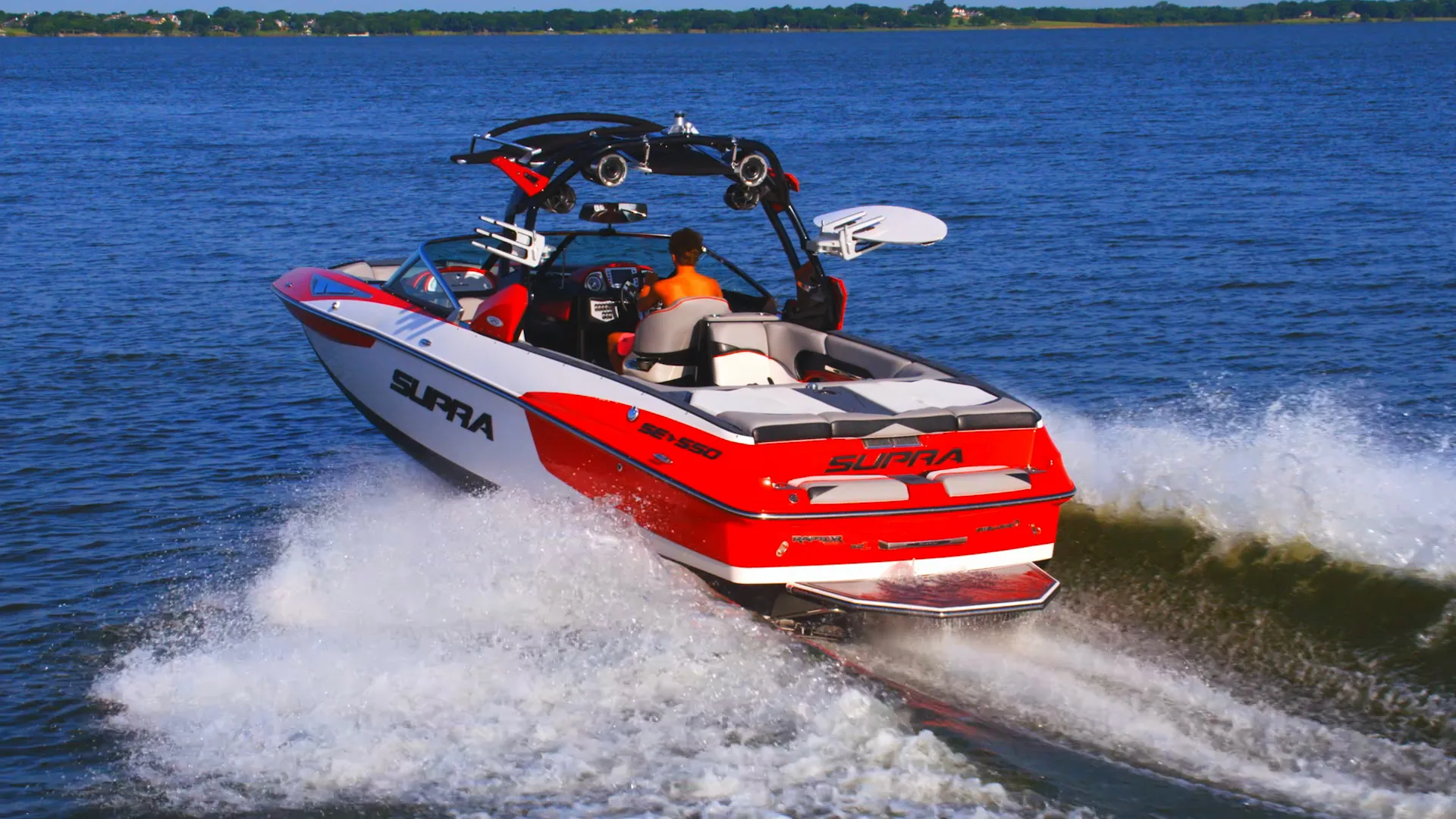 The red and white Supra SE550 running hard on blue water, throwing spray