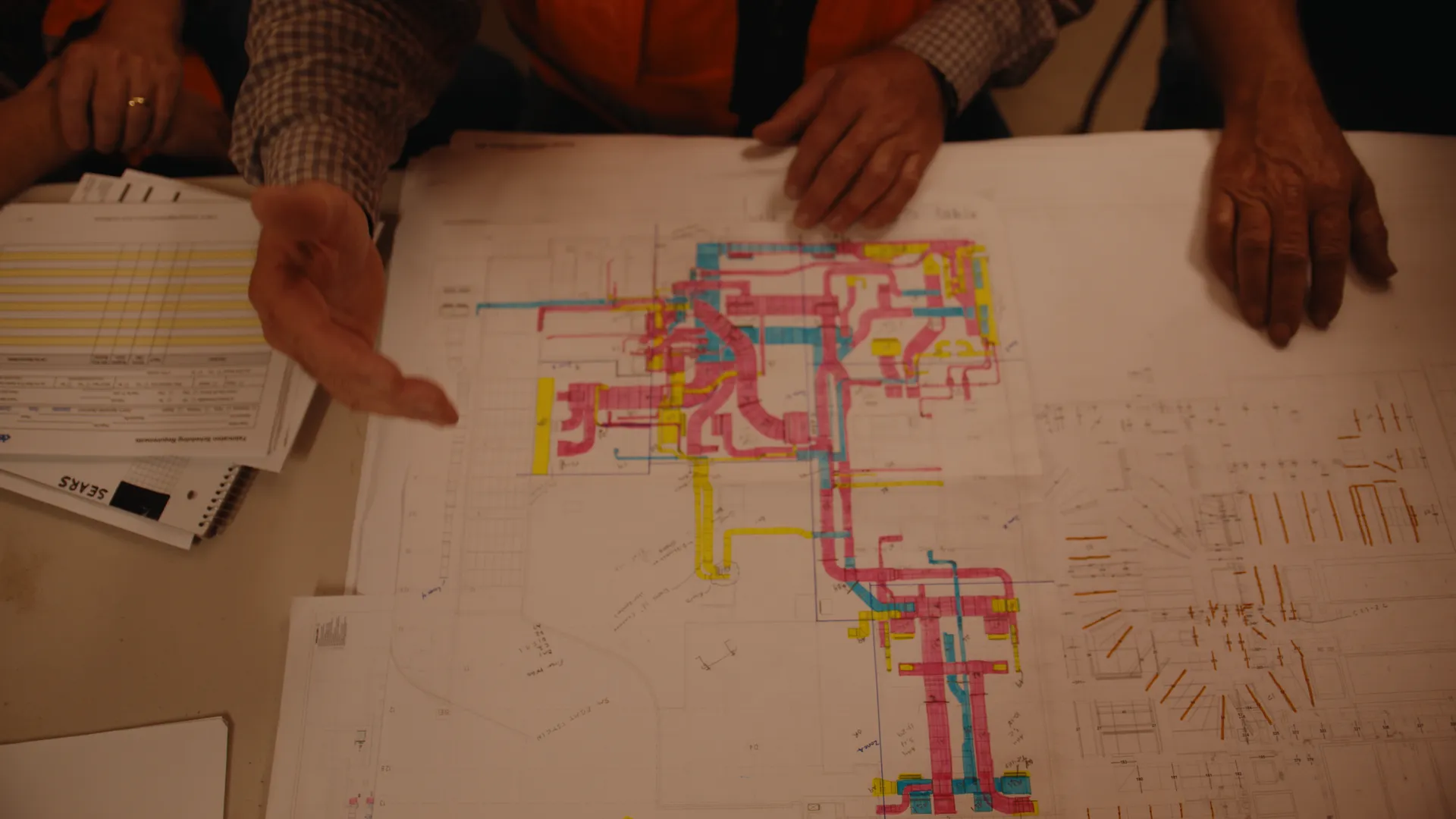 Hands spread across color-coded mechanical plans