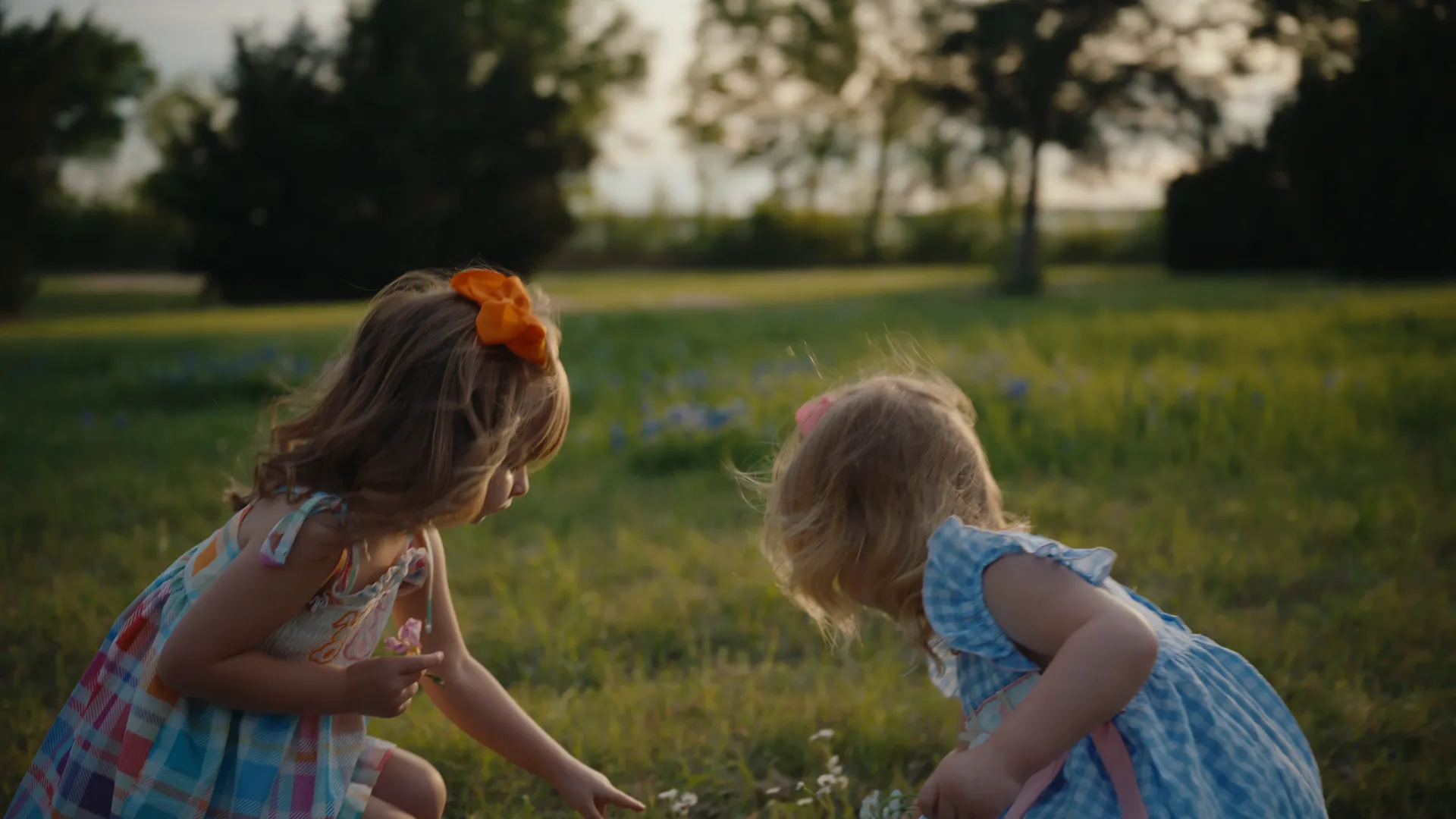 Two little girls crouched in the grass picking wildflowers
