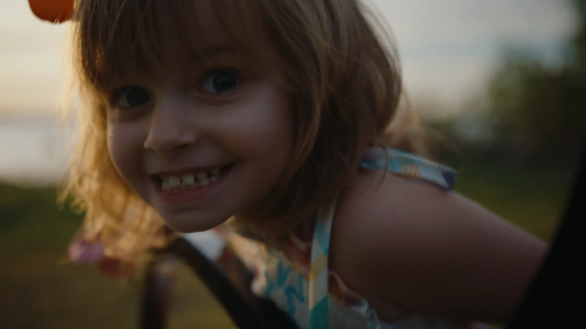 A grinning girl leaning into the lens, backlit by the setting sun