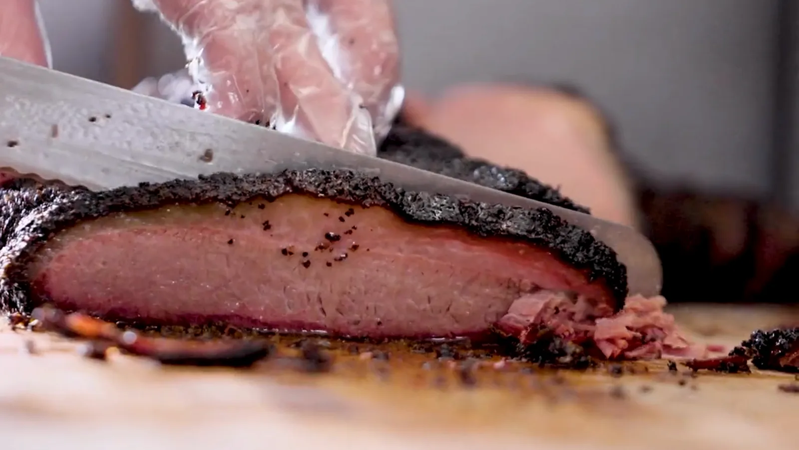 Knife slicing smoked brisket with a dark bark