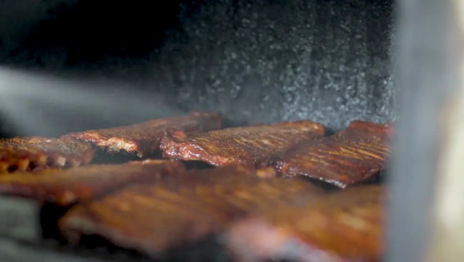 Ribs on the smoker grate in backlit smoke