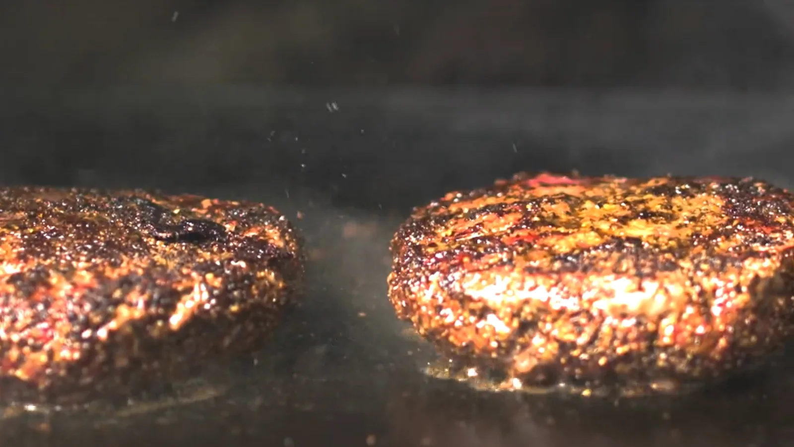 Two burger patties sizzling on the griddle