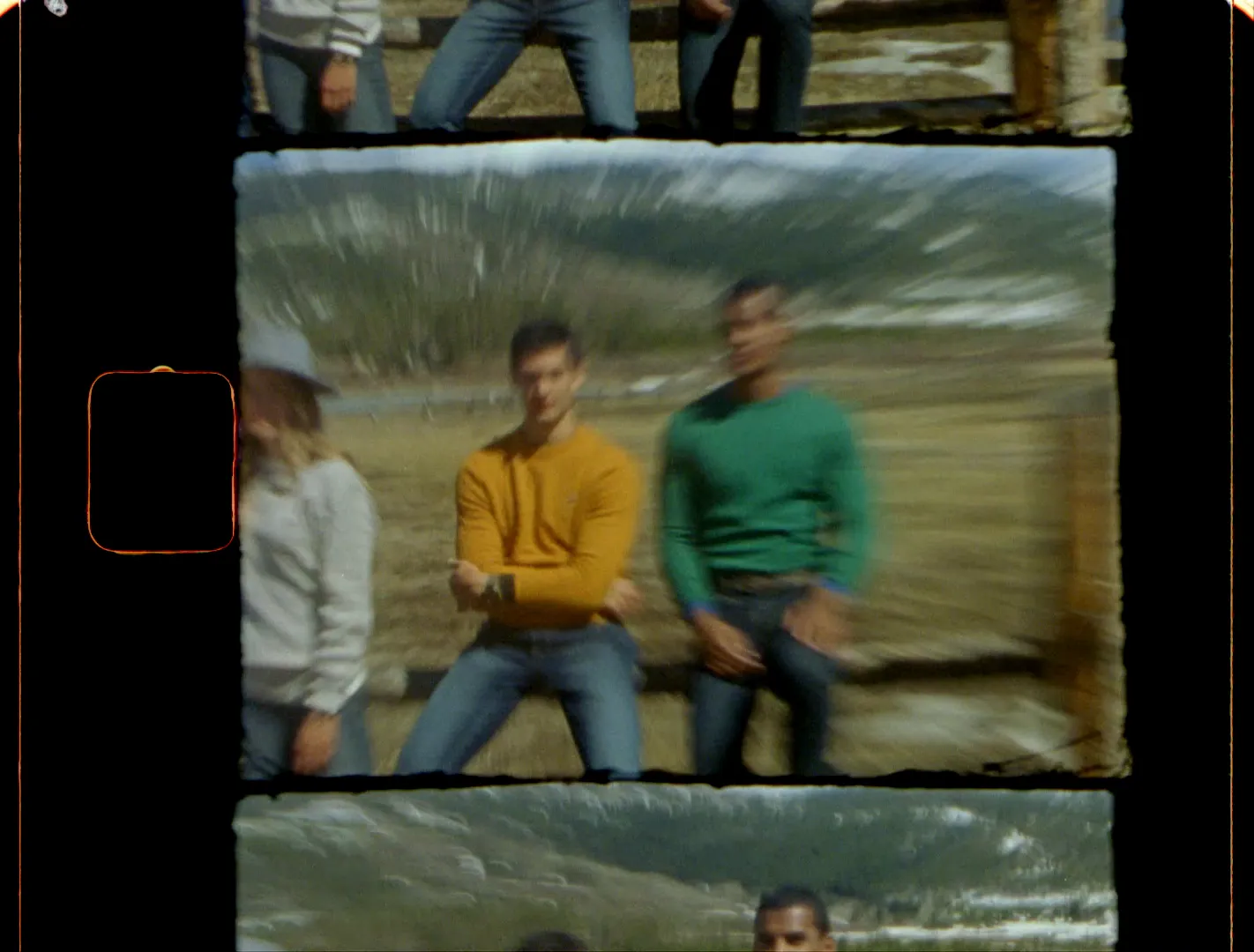 Friends in bright sweaters sitting on a buck-and-rail fence below snowy Colorado peaks, in a Super 8 frame