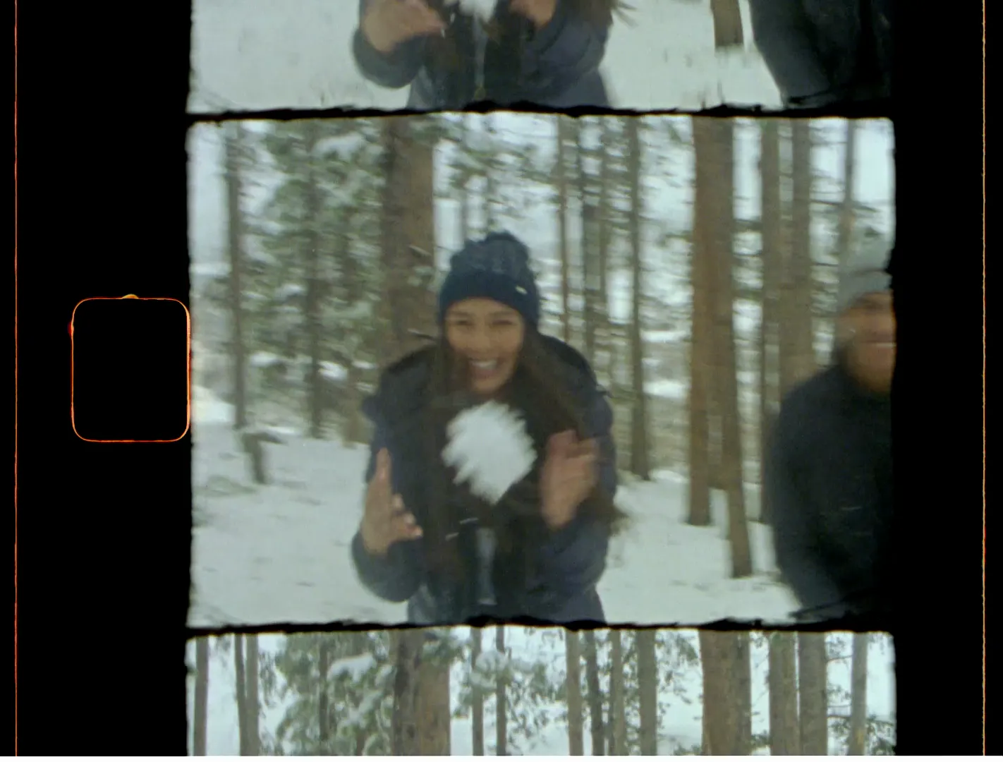 A woman in a knit beanie laughing with a snowball in a snowy pine forest