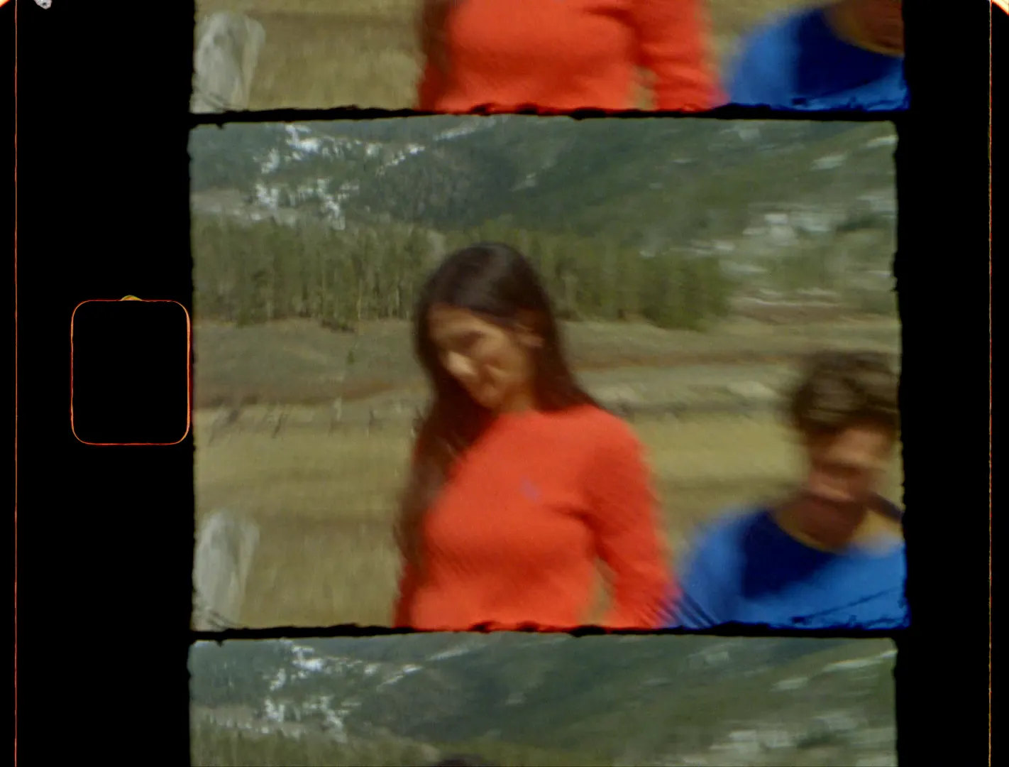 A woman in a red sweater walking through a mountain meadow