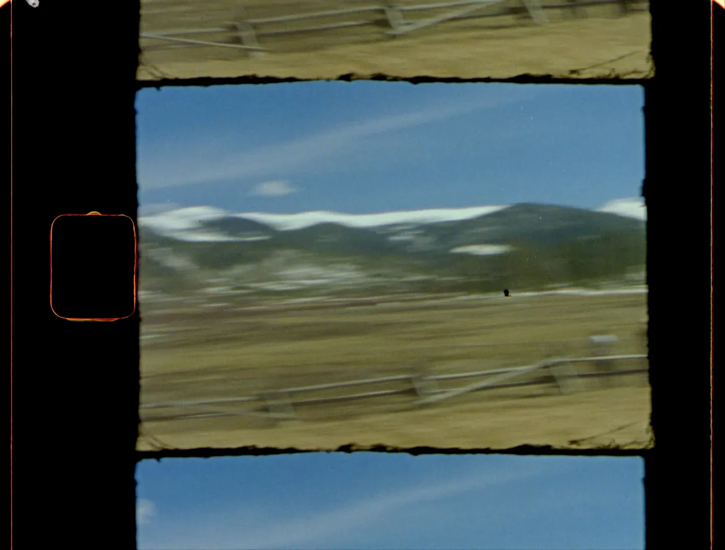 A wide mountain valley lined with split-rail fences and snowy ridges