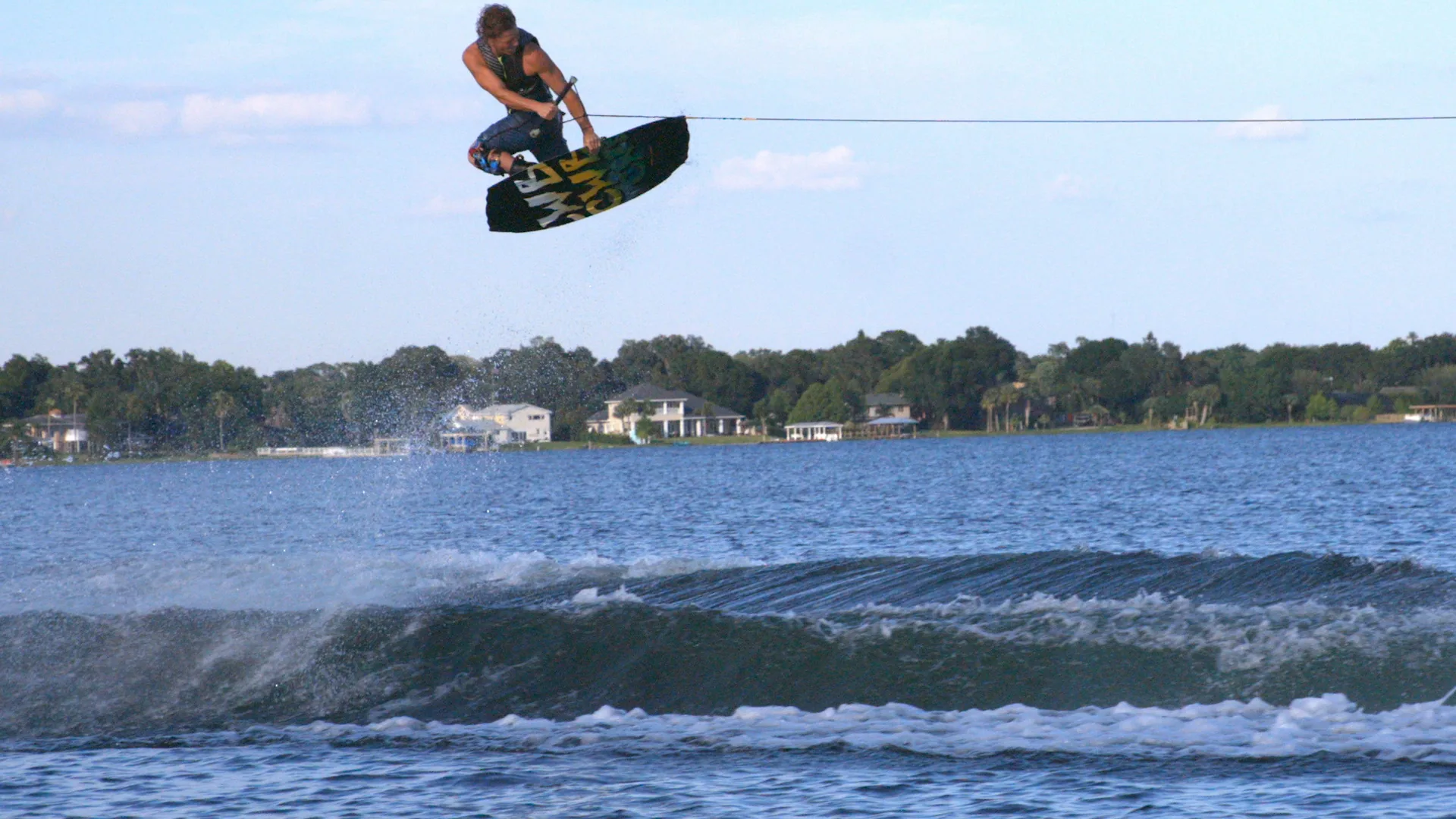 Mike Dowdy boosting a method grab high above the wake, lakeside houses on the shore