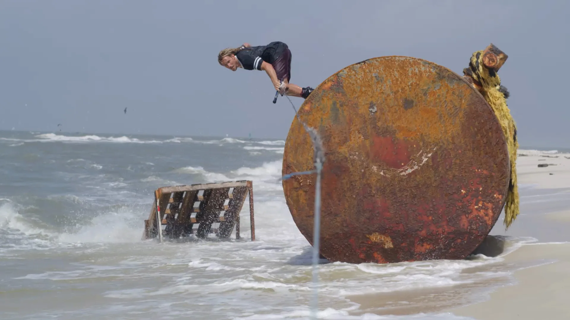 Alex Graydon sailing over a rusted barrel with a painted smile on a stormy Gulf Coast beach